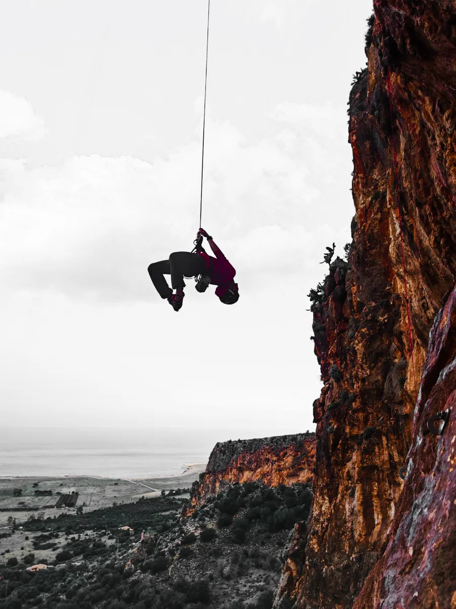Rox hanging upside down on a rope above the sea